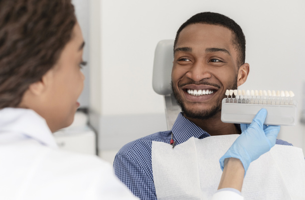 Веселый африканский пациент и стоматолог выбирают оттенок наполнения
 - Фото, изображение