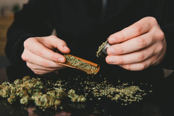 Man rolling a marijuana weed blunt. Close up of addict lighting up marijuana joint with lighter. Man preparing and rolling marijuana cannabis joint. - Valokuva, kuva