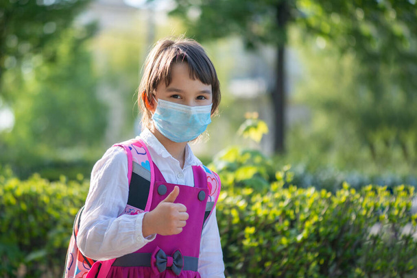Piccola ragazza della scuola che torna a scuola dopo un'epidemia di pandemia con indosso una maschera facciale
 - Foto, immagini