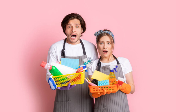 Huishoudelijke taken. Portret van geschokte paar Holding Emmers met schoonmaak benodigdheden - Foto, afbeelding