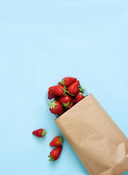 Fresh strawberries in a paper bag on a blue background. Shopping View from above. - Foto, imagen
