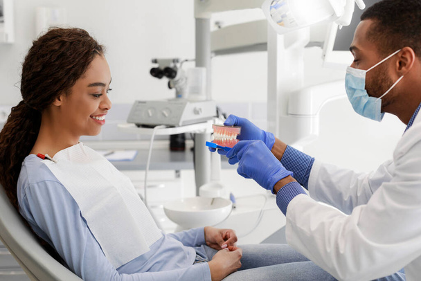 Czarny dentysta pokazuje pacjentce plastikową szczękę - Zdjęcie, obraz