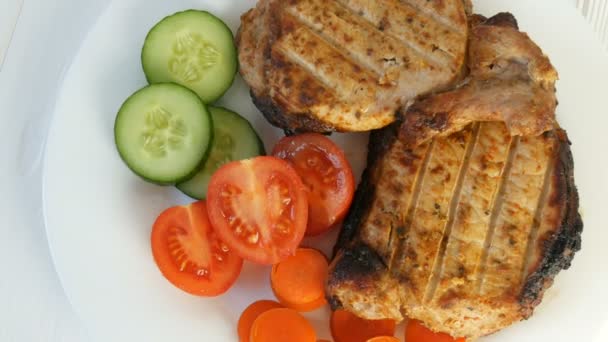 焼きステーキのおいしいジューシーな新鮮なスライスは、白レストランプレート上のチェリートマトと新鮮な野菜キュウリの横に豚肉の肉を濃縮します。 - 映像、動画