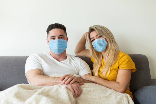 Young casual couple wearing face mask for avoid Covid-19 contagion. Coronavirus quarantine at home concept. - Фото, изображение