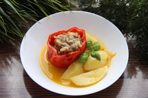 Фаршированный перец с картошкой, украшенный базиликом на плоской тарелке
 - Фото, изображение