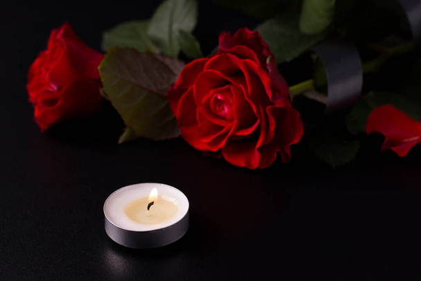 Czerwone kwiaty na czarnym tle obok świec. Koncepcja śmierci i żałoby. Przestrzeń kopiowania - Zdjęcie, obraz