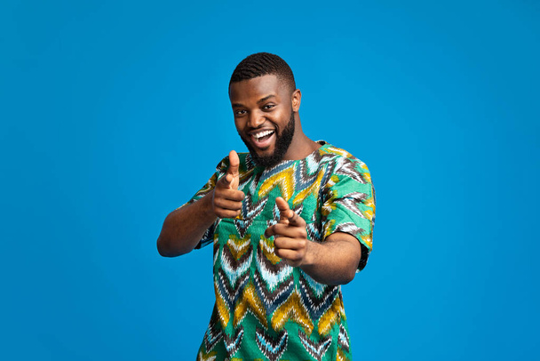 Веселый черный парень в традиционной африканской одежде указывает на камеру
 - Фото, изображение