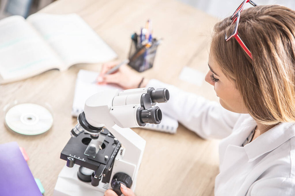 Female laboratory technician writing down observations from work with a microscope. - Zdjęcie, obraz