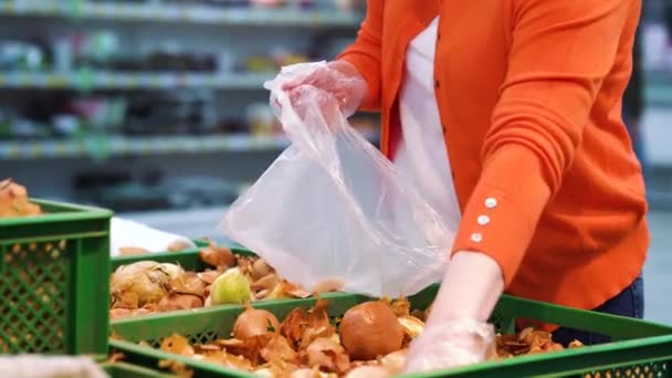 Crop woman in plastic gloves picking onions at grocery store - Filmagem, Vídeo