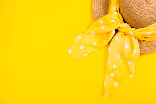 Een strohoed met een stippen sjaal op een gele achtergrond met een lege plek voor reclame en tekst. Bovenaanzicht. - Foto, afbeelding