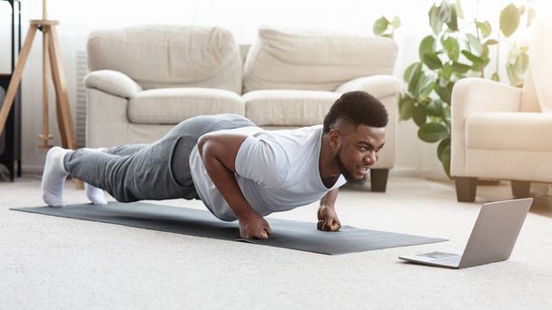 Sportowy czarny człowiek co pięść deska ćwiczenia przed laptopem - Zdjęcie, obraz
