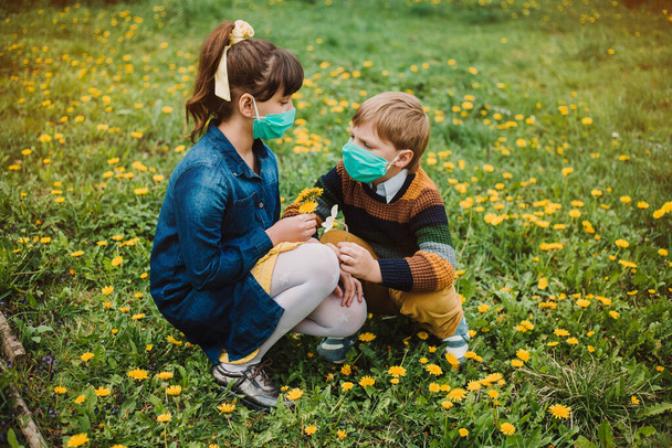 Kinderen met medische maskers verzamelen paardebloemen in de tuin. Het concept van bescherming tegen coronovirus en sociale afstand - Foto, afbeelding