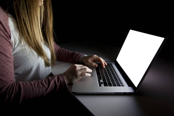 The young woman sitting in the dark living room and working with laptop - Фото, изображение