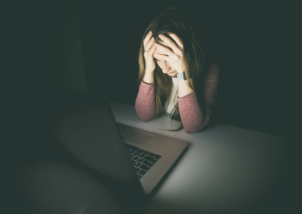 非常に疲れて疲れ女性は、手をノートパソコンで夜遅くに座って彼女の頭を保持します。労働、過労、不安の概念 - 写真・画像