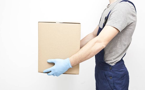The courier is holding the carton box in his hand wearing  protective latex gloves on the gray background - Fotoğraf, Görsel