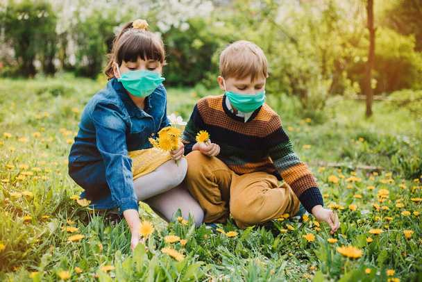 Boy and girl wearing a medical mask, flowers on the background. Children in a protective mask. Warning of the dangers and safety quarantine measures against COVID-19. - Foto, Bild