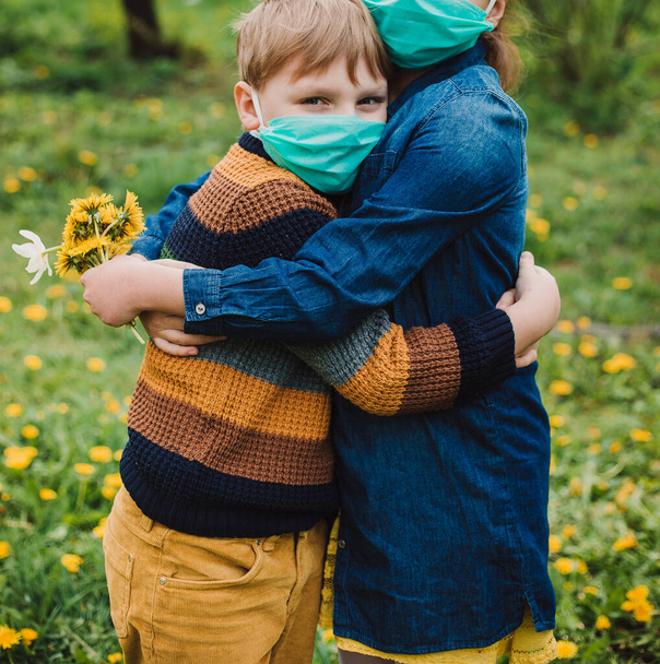 男の子と女の子の医療マスクを着て、背景に花。保護マスクの子供たち。危険性の警告とCOVID-19に対する安全検疫措置.コロナウイルスのパンデミック. - 写真・画像