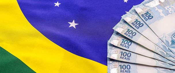 600 Brezilya reaisi, 100 reais banknotla birlikte, arkasında Brezilya bayrağı var. Brezilya 'daki ekonomik krizin imajı. - Fotoğraf, Görsel