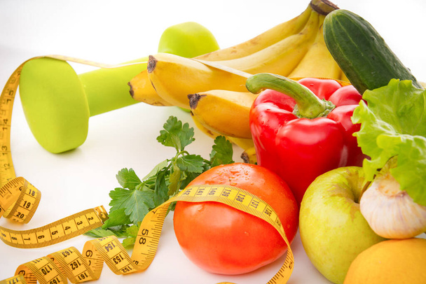 fresh fruits and vegetables with dumbbells and measuring tape on a white background, healthy food, peppers, bananas, Apple, greens,  tomato, cucumber,  - Foto, Imagen