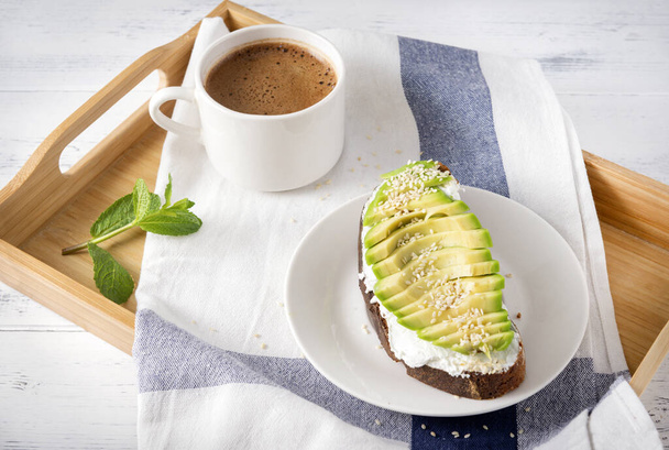 1 avocado and cheese sandwich on a plate, a Cup of black coffee on a towel on a tray on a white wooden background, Breakfast - Foto, Bild