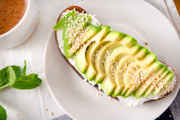 1 avocado and cheese , sesame sandwich on a plate, Cup of  coffee on a towel , Breakfast - Photo, Image