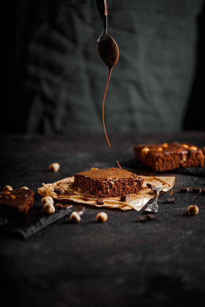 Dark chocolate and cocoa brownie cake on light gray concrete table, pieces of chocolate and hazelnut - Fotografie, Obrázek