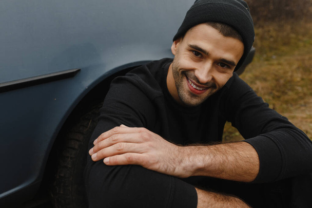 Smaling man in the black hat sitting near his car. Man portrait - 写真・画像