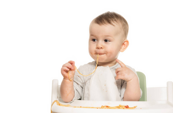 Porträt eines lustigen Jungen, der Spaghetti in Tomatensauce auf weißem Hintergrund isst.  - Foto, Bild