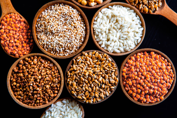 Bowls of various cereals. Various kinds of natural grains and cereals. Different types of groats in bowls on a black background. Healthy nutrition food - Foto, afbeelding