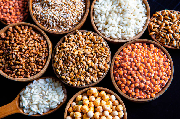 Tigelas de vários cereais. Vários tipos de grãos naturais e cereais. Diferentes tipos de grumos em tigelas em um fundo preto. Alimentação nutricional saudável
 - Foto, Imagem