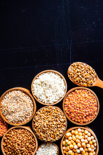 Tigelas de vários cereais. Vários tipos de grãos naturais e cereais. Diferentes tipos de grumos em tigelas em um fundo preto. Alimentação nutricional saudável
 - Foto, Imagem