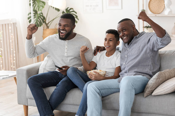 Alegre familia negra, padre, abuelo e hijo viendo el partido de fútbol en la televisión
 - Foto, imagen