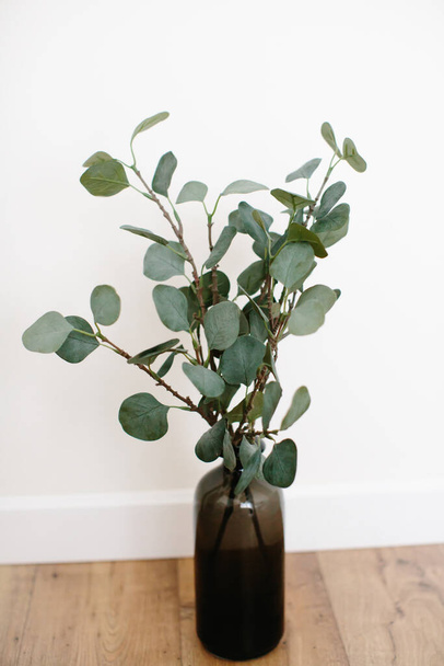 Branches de plantes vertes artificielles sont recueillies dans un bouquet, se tenir dans un vase en verre sombre sur un fond clair
. - Photo, image
