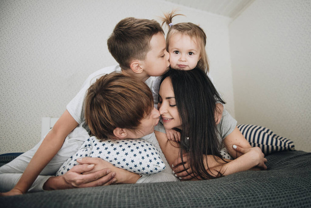 パジャマを着て家にいる家族。娘と息子。朝起きてください。ベッドの上の寝室で抱擁とキス. - 写真・画像