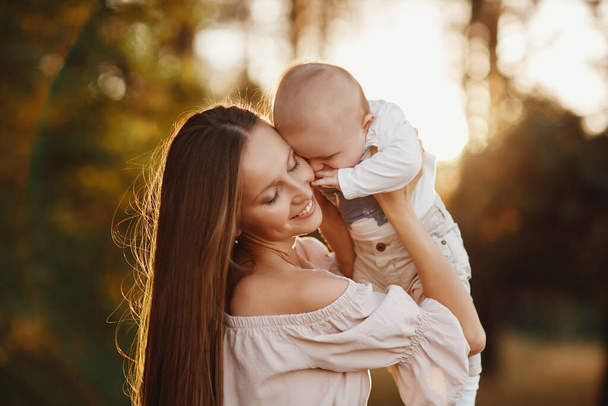 Happy child and his mom have fun outdoors in a field flooded with . Mom holds the child in her arms, and the child hugs and kisses the mother. Mother's Day. selective focus. - Foto, Bild