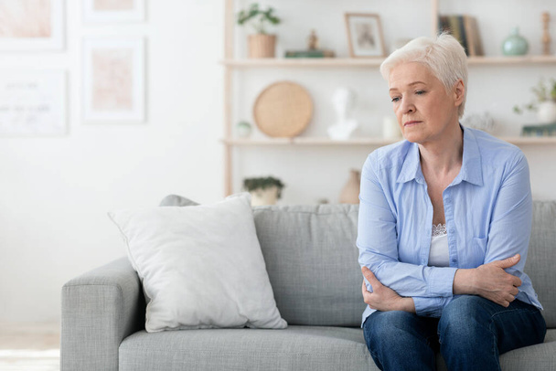 Egy depressziós idős nő portréja, aki otthon ül a kanapén. - Fotó, kép