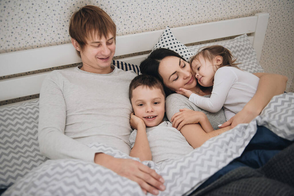 Family at home in pajamas. Daughter and son. Wake up in the morning. Hugging and kissing in the bedroom on the bed. - 写真・画像