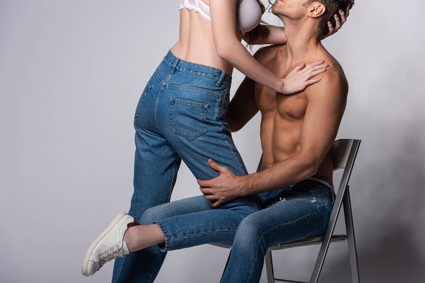 cropped view of seductive girl in bra touching muscular man sitting on grey  - Fotografie, Obrázek