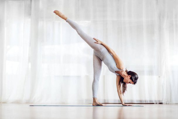 Aantrekkelijke jonge brunette in Half Moon yoga positie. Yoga studio interieur. - Foto, afbeelding