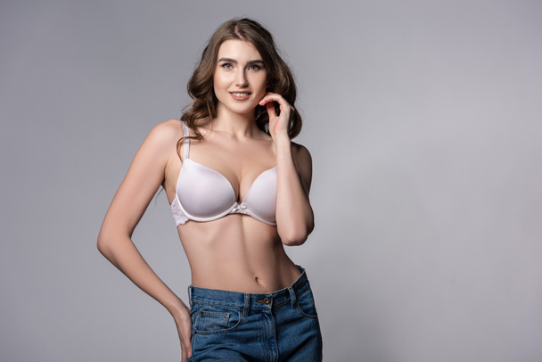 smiling girl in bra and denim jeans standing on grey  - Foto, immagini