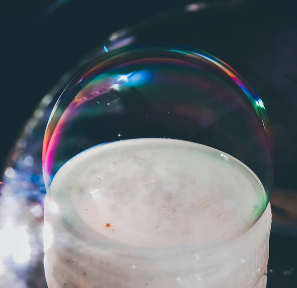Burbuja de jabón que refleja los colores del arco iris en un fondo negro
 - Foto, Imagen