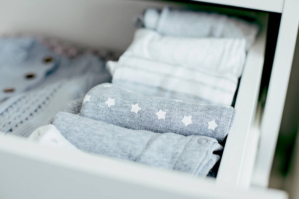 Baby- oder Neugeborenensachen in weißen, blauen und grauen Farben liegen in der Schublade. Lady Fliegensystem, Kondo, Konsumkonzept. Lebensstil zu Hause. - Foto, Bild