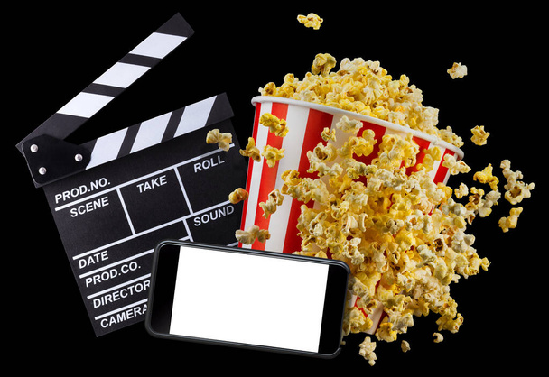 Flying popcorn, film clapper board and phone isolated on black background, concept of watching TV or cinema. - Foto, imagen