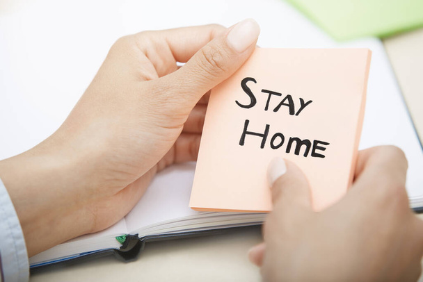Manos sosteniendo una nota adhesiva rosa con texto Stay Home
 - Foto, Imagen