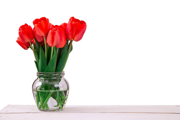 Bouquet of fresh red tulips in glass vase on wooden table, isolated on white background - 写真・画像