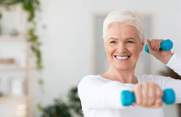 Retrato de feliz anciana haciendo ejercicio con sombrillas en casa
 - Foto, Imagen