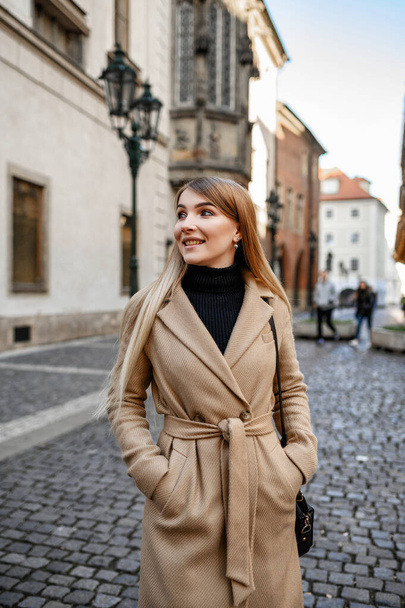 Attractive blonde in a beige coat walks around the old town - Φωτογραφία, εικόνα