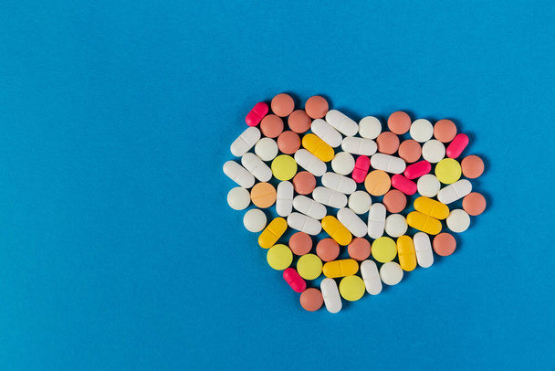 Many different pills and tablets folded in shape of heart on blue background. Many pills and tablets with space for text. Health care. Top view. Copy space. New image. Pharmaceutical picture. Closeup - Fotoğraf, Görsel