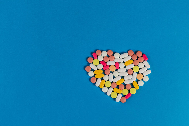 Wiele różnych tabletek i tabletek złożone w kształcie serca na niebieskim tle. Wiele tabletek i tabletek z miejscem na tekst. Opieka zdrowotna. Widok góry. Odbiór. Nowy wizerunek. Obraz farmaceutyczny - Zdjęcie, obraz