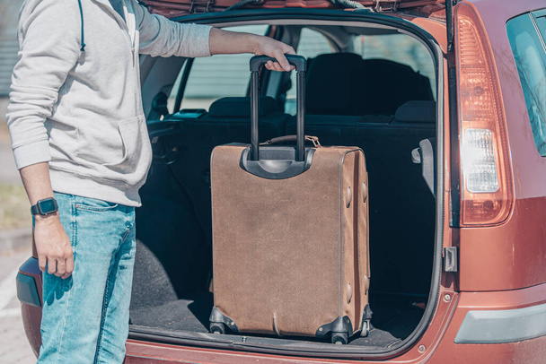 The young man pulls luggage from the car trunk - Photo, Image